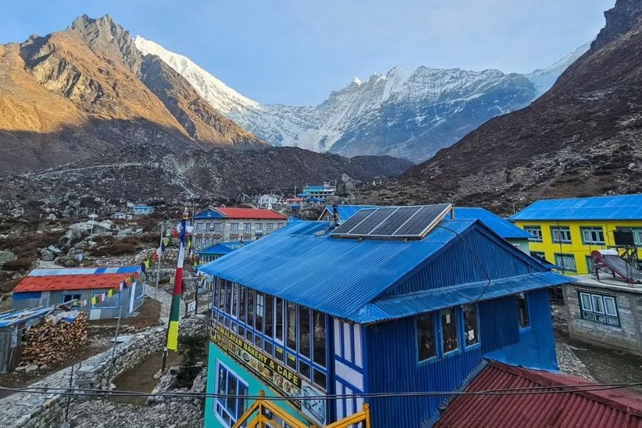 Colorful teahouse lodges with blue roofs and solar panels at Kyanjin Gompa in Langtang Valley with glacier peaks behind